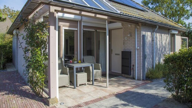 Een overdekt terras met glazen wanden, rieten meubilair en een pad van bakstenen.