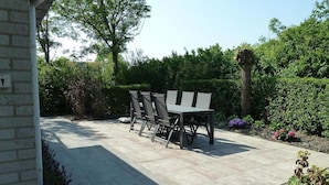 Een terras met een tafel en stoelen, omgeven door groen en een bakstenen muur.
