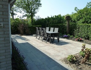 Eine Terrasse mit Tisch und Stühlen, umgeben von viel Grün und einer Backsteinmauer.