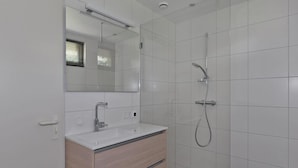 Een moderne badkamer met een wit wastafelmeubel, een grote spiegel, een douche met een handdouche en betegelde wanden.