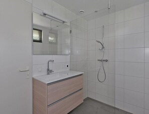 Ein modernes Badezimmer mit einem weißen Waschtisch, einem großen Spiegel, einer Dusche mit Duschbrause und gefliesten Wänden.
