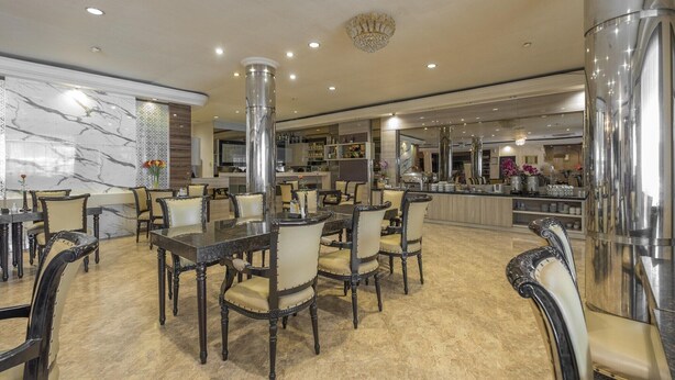 A spacious dining area with marble walls, a chandelier, and a bar area in the background.