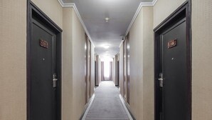 A hotel hallway with doors on both sides, a carpeted floor, and a ceiling light. - Twin Escape Near Losari Beach (Makassar)
