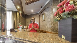 A hotel reception area with a marble counter, a man in a red shirt, a flower arrangement, and a framed certificate on the wall. - Twin Escape Near Losari Beach (Makassar)