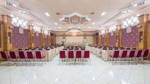 A large conference room with rows of tables and chairs, a stage, and a chandelier. - Twin Escape Near Losari Beach (Makassar)