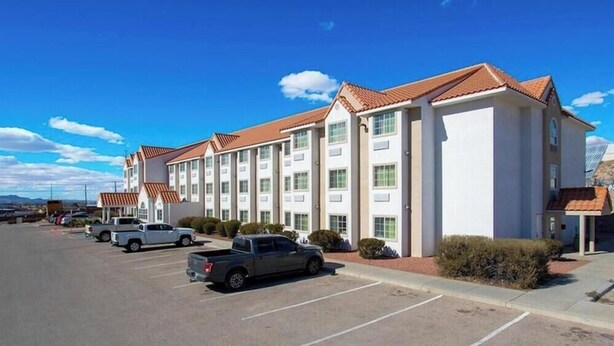 Un hotel de varios pisos, un estacionamiento con varios vehículos y un cielo despejado.