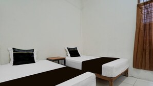 A room with two single beds, each with a pillow and a brown bedspread, a small wooden nightstand, and a window with brown curtains.