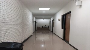 A hallway with a white brick wall, a black suitcase on a wooden surface, and a door with a number sign. - Single Room near Cihampelas Walk (Bandung)
