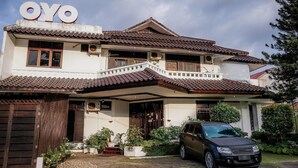 A two-story house with a tiled roof, a balcony, and a car parked in the driveway.