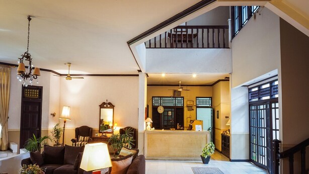 A spacious living area with a sofa, coffee table, and lamp, leading to a reception desk and a staircase.