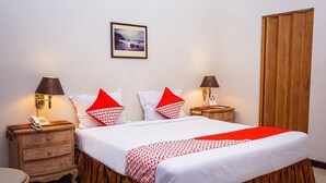 A neatly made bed with red and white bedding, two bedside tables with lamps, a wooden wardrobe, and a framed picture on the wall.