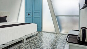 A room with a bed, a blue door, a kettle, and a tiled floor.
