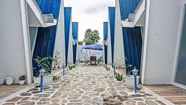 A stone-paved courtyard with a central seating area, flanked by blue curtains and potted plants.