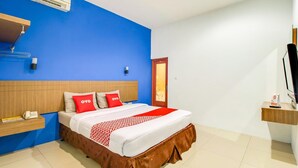 A hotel room with a bed, a bedside table with a phone, a wall-mounted air conditioner, and a door.