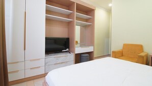 Un dormitorio con cama, televisor, una silla y almacenaje integrado.