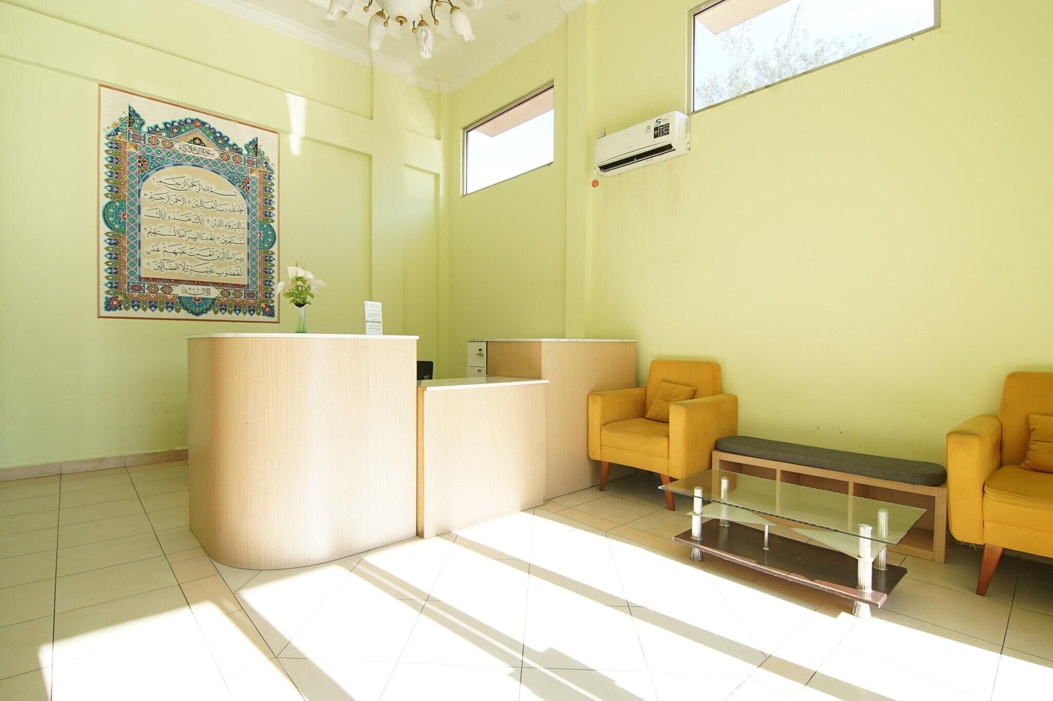 Zona de recepción con mostrador, dos sillas amarillas, una mesa de vidrio y un elemento decorativo en la pared.