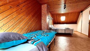 Um quarto com teto inclinado, cama com colcha estampada, um banquinho e uma parede de tijolos.