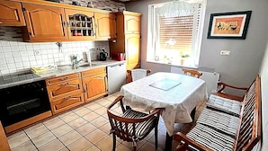 Uma cozinha com armários de madeira, uma mesa de jantar com cadeiras e uma janela com persianas.