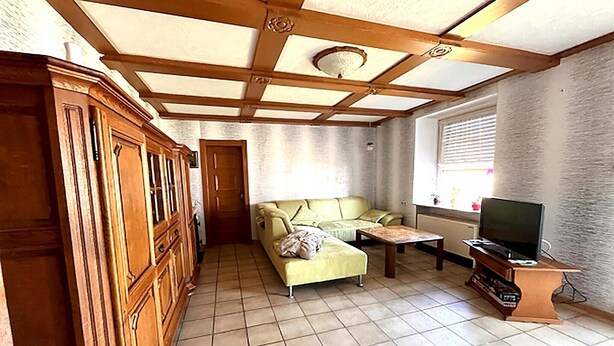 Sala de estar com sofá, televisão, armário de madeira e chão ladrilhado.
