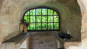 Ein raum mit steinernen Wänden, einem großen Bogenfenster, einer Bank und einem Tisch mit Laptop und Ladegerät.