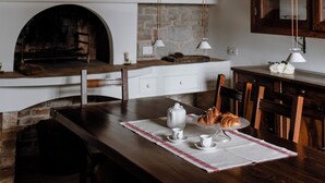A rustic interior with exposed wooden beams, a stone fireplace, and a dining area with a white table set for two.