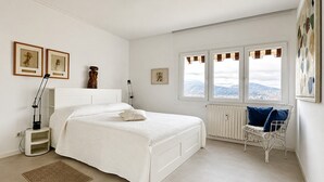 Um quarto com uma cama, uma cadeira, um radiador e uma janela com vista.