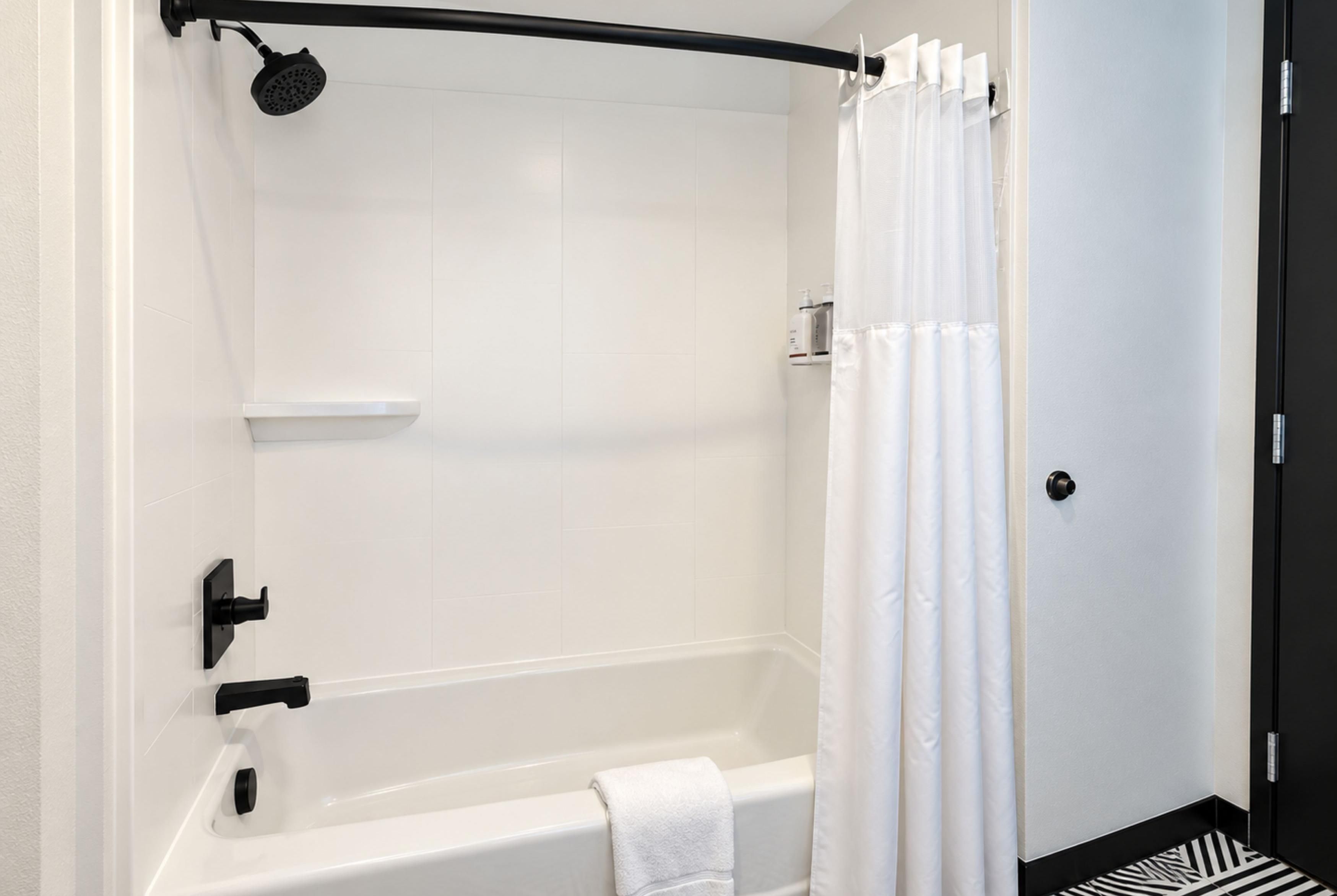 Une salle de bain moderne avec une baignoire blanche, une pomme de douche et un rideau de douche blanc.