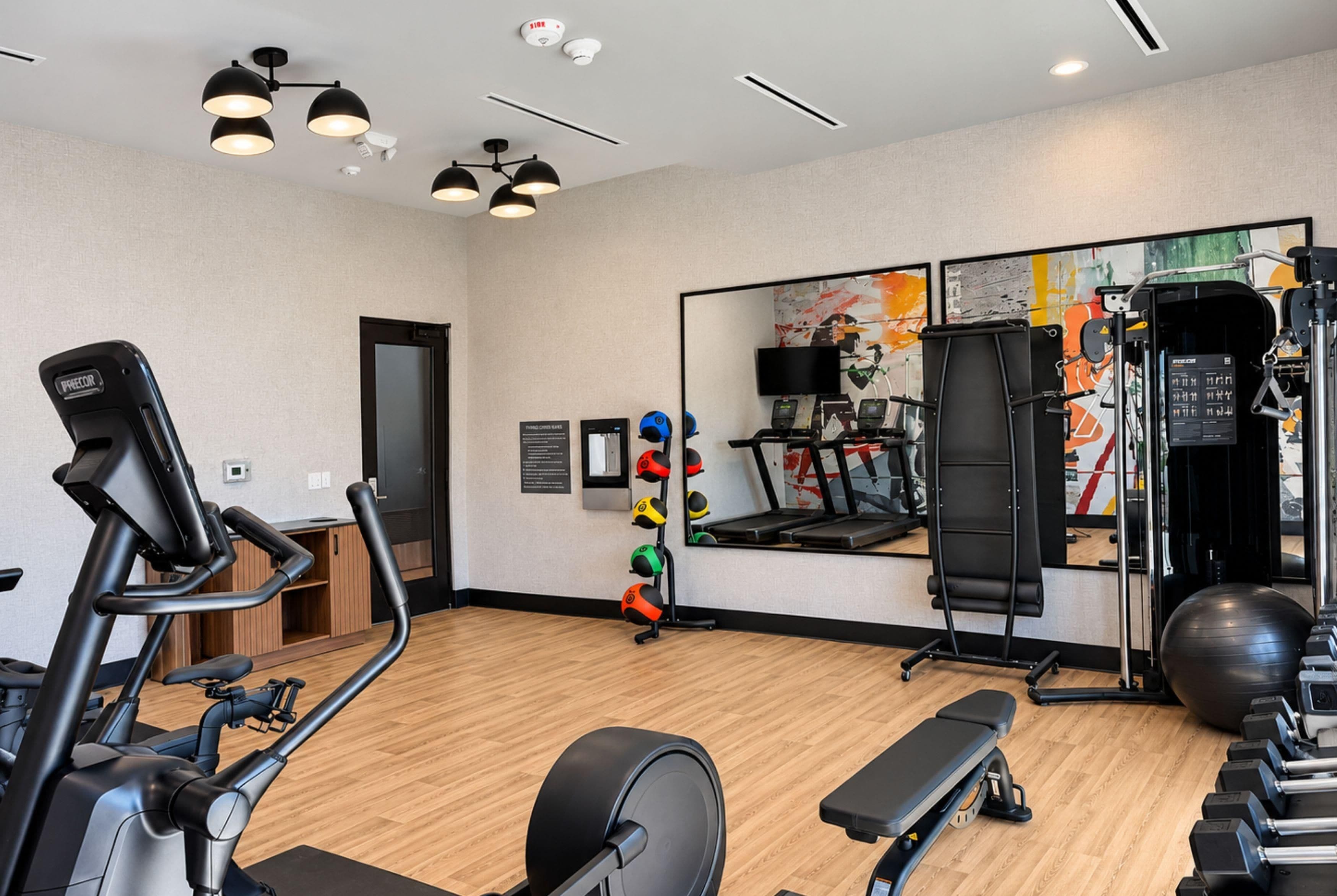 Un gimnasio con equipamiento de ejercicio, un espejo y suelo de madera.