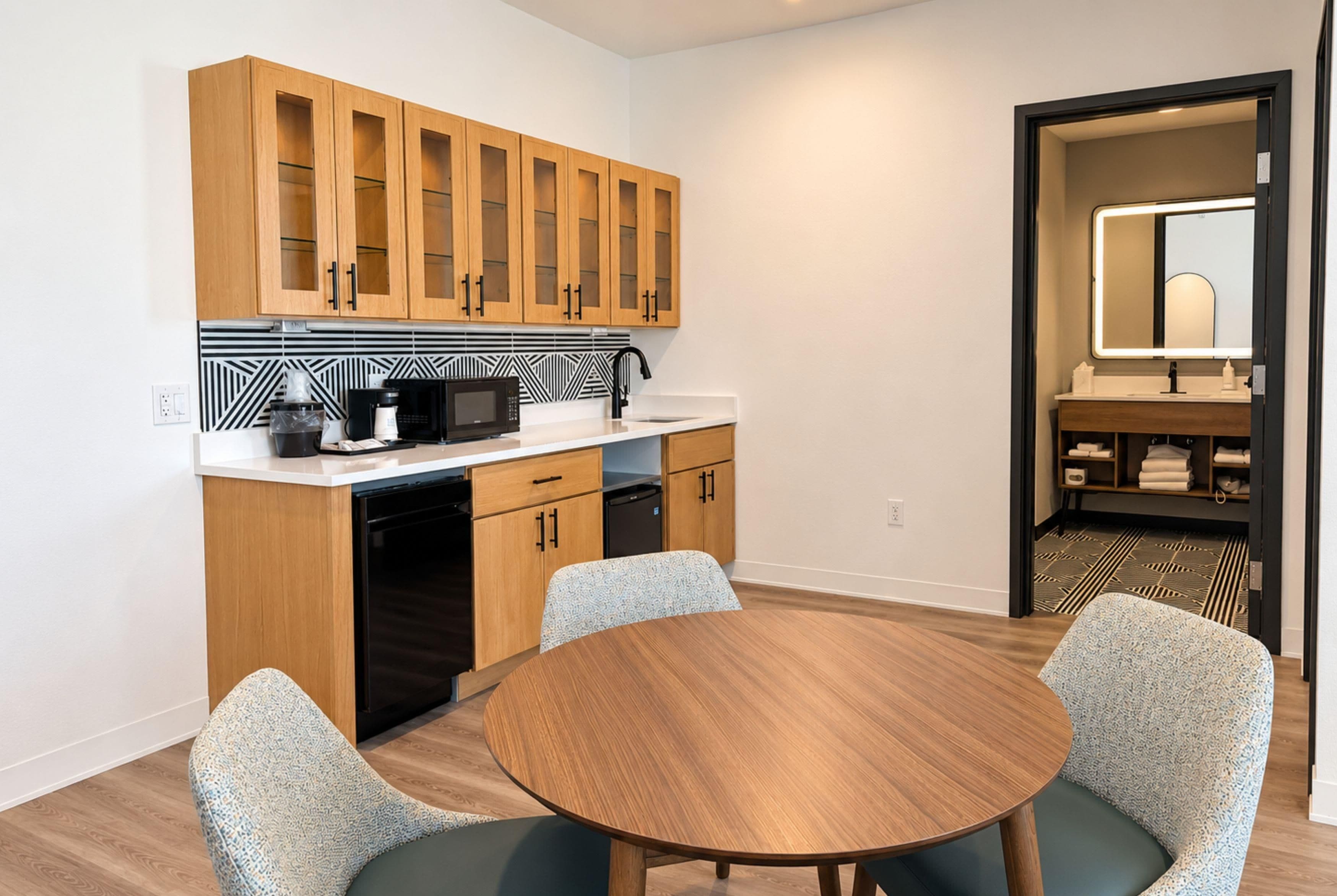 A compact kitchen with wooden cabinets, a microwave, and a dishwasher. There is a round table with two chairs in the center.