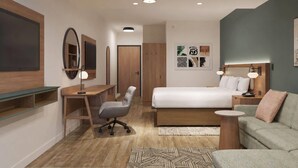 A modern bedroom with a bed, desk, chair, and a small sofa. - La Quinta Inn and Suites by Wyndham Central McKinney (McKinney)