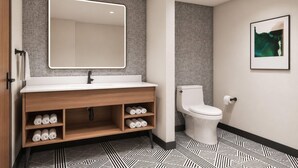 A modern bathroom with a wooden vanity, a large mirror, a toilet, and patterned flooring. - La Quinta Inn and Suites by Wyndham Central McKinney (McKinney)