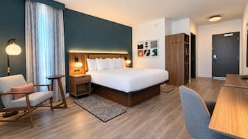 A modern hotel room with a large bed, bedside tables, a desk, a chair, and a wardrobe.