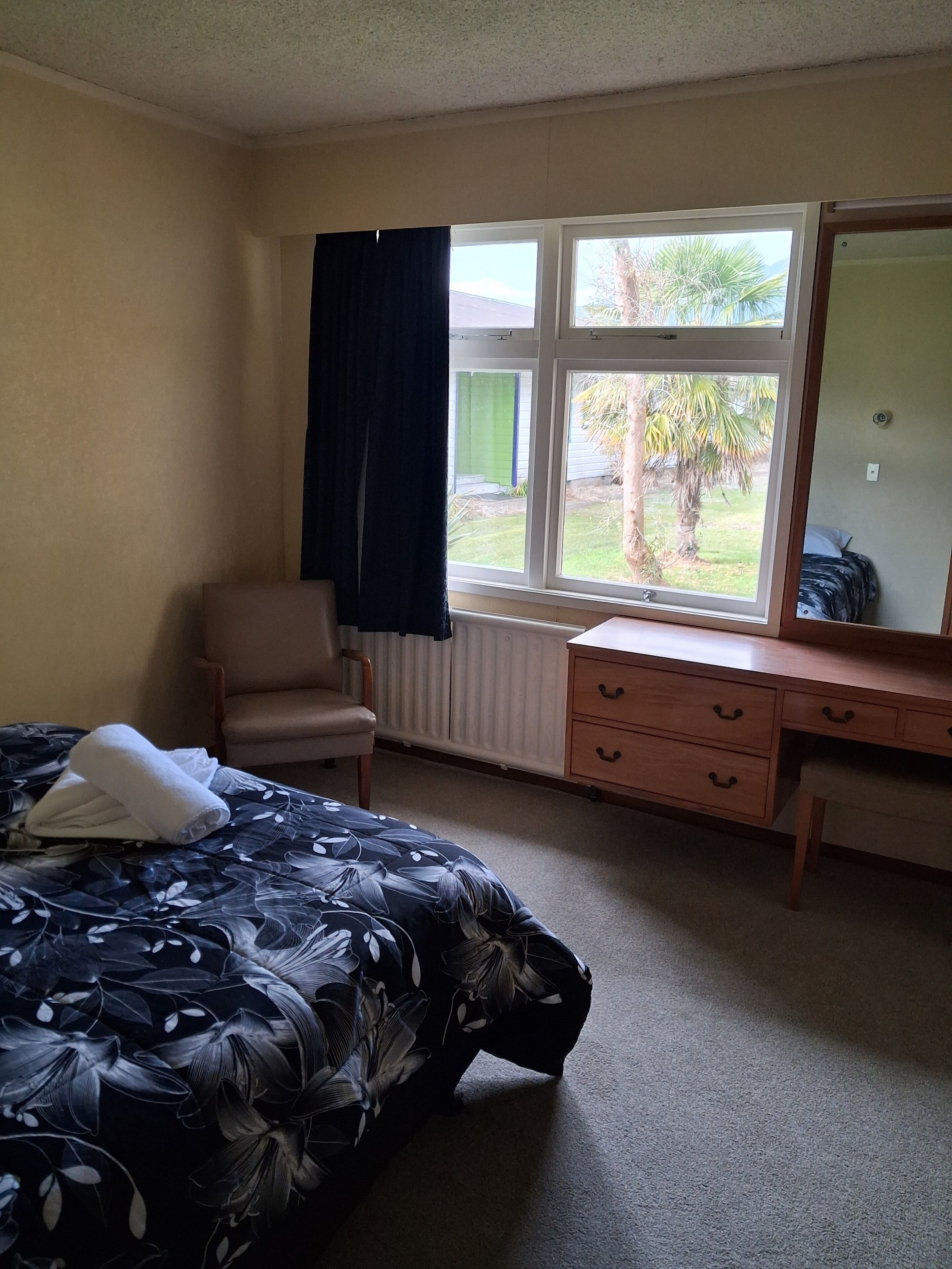 Habitación de hotel con cama, una silla, un escritorio, un espejo y ventana con vistas al exterior.