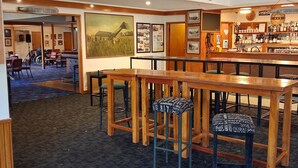 Una zona de bar con mesas y sillas de madera, adornos de ciervo en el techo y una barra con diferentes botellas.