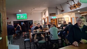 Un bar con clientes, un televisor mostrando un evento deportivo y un letrero que indica el baño de hombres.