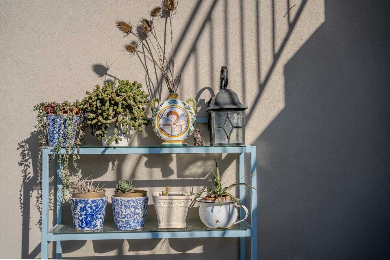 A blue metal shelf with potted plants and a decorative item against a wall.