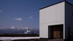 A modern building with a large garage door, set against a backdrop of snow-capped mountains. - monel (Nakafurano)