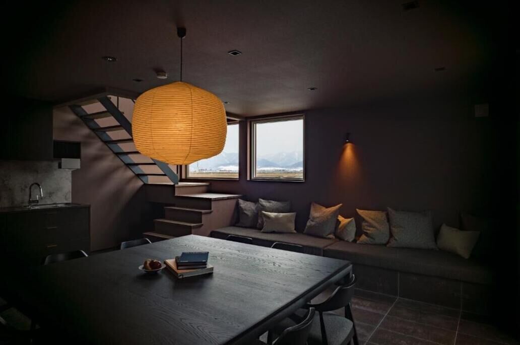 Et moderne interiør med spiseplads, sofa, trappe og store vinduer.