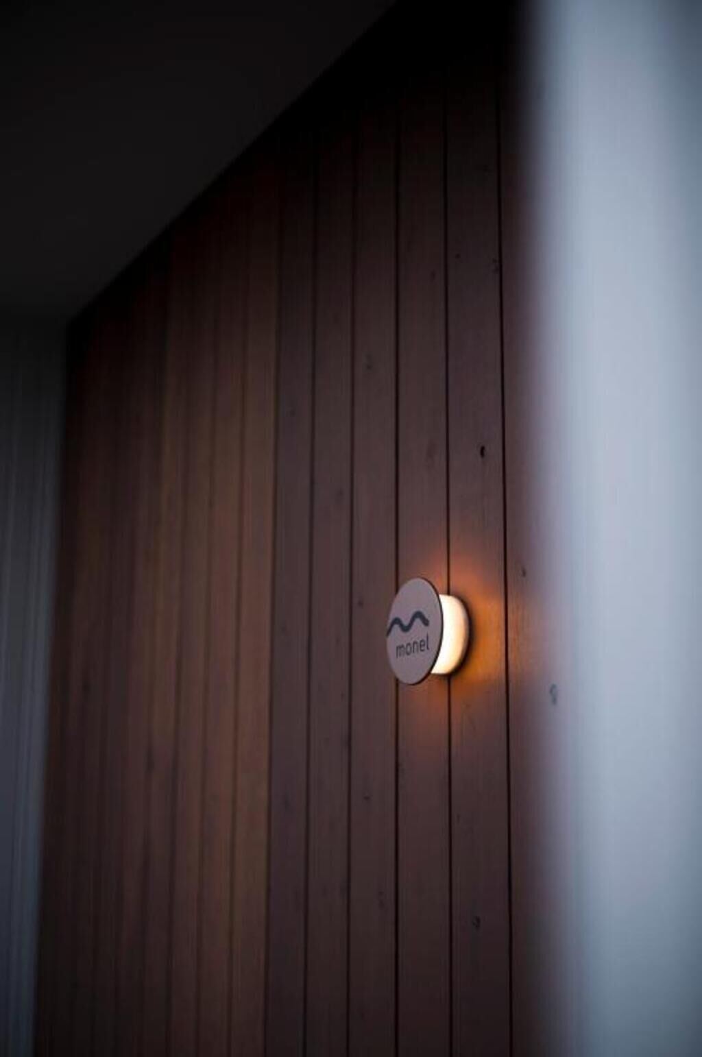 Pared de madera con una lámpara circular etiquetada 'monel'.