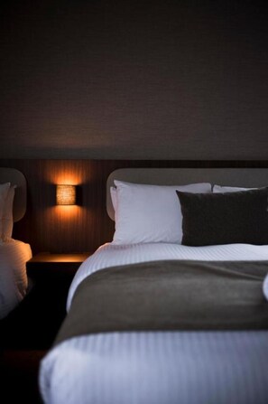 Une chambre d’hôtel avec un lit, des oreillers, une table de chevet et une lampe fixée au mur.
