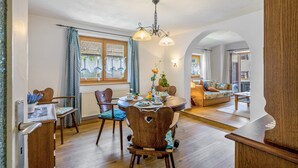 Un espace repas comprenant une table ronde, des chaises, un lustre et une vue sur le salon, accessible par une arche.