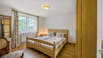 Ein Bett aus Holz in einem Raum mit Holzboden, einem Stuhl, einem Nachttisch mit Lampe und einem Fenster mit Vorhängen.