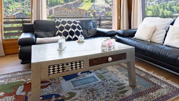 Ein modernes Wohnzimmer mit einem großen Fenster, einem schwarzen Ledersofa, einem Couchtisch und einem gemusterten Teppich.