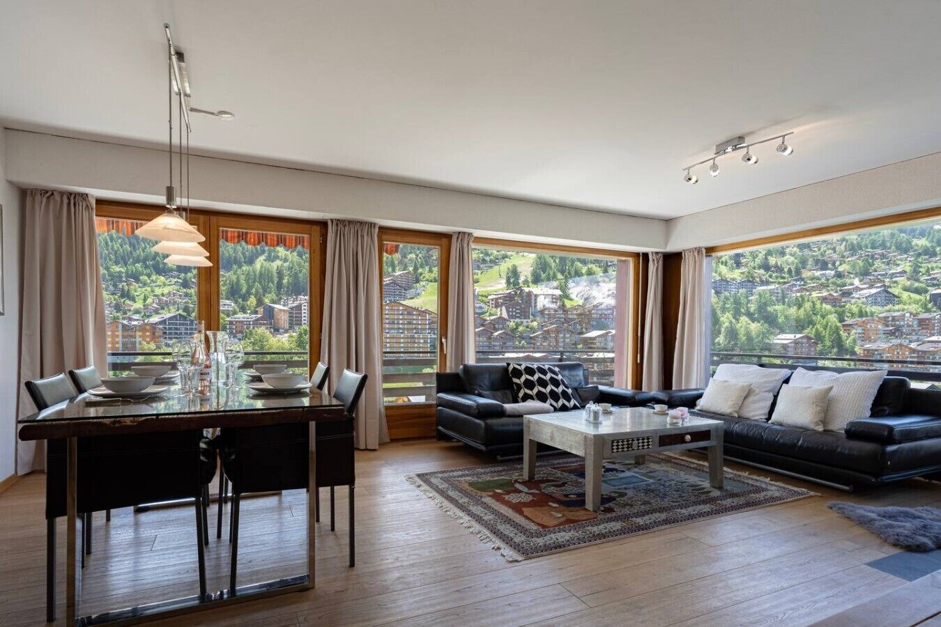A modern living room with a dining area, large windows, and a view of a mountainous landscape.