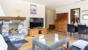 Ein Wohnzimmer mit Kamin aus Stein, einem Flachbildfernseher, einem Holzkabinett und einem Essbereich mit Stühlen und Tisch.