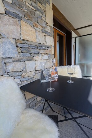 A stone wall, a table with two wine glasses, and a bottle on a white furry ottoman. - Panoramic view, 2 bedrooms, covered parking (Nendaz)