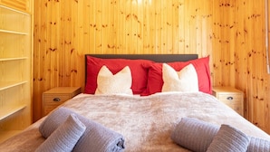 Ein Zimmer mit Holzwänden, einem Bett, roten und weißen Kissen und einer Decke.