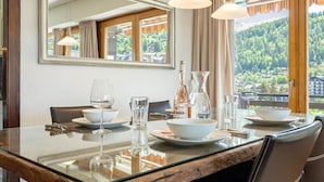 Ein Essbereich mit Glastisch, Stühlen und Blick auf eine gebirgige Landschaft durch große Fenster.