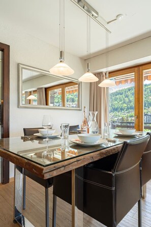 A dining area with a glass table, chairs, and a view of a mountainous landscape through large windows. - Panoramic view, 2 bedrooms, covered parking (Nendaz)