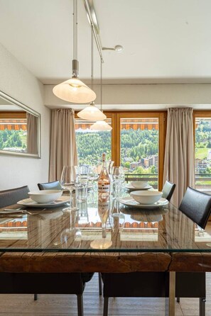 A dining area with a glass table, chairs, and a bottle of wine. - Panoramic view, 2 bedrooms, covered parking (Nendaz)